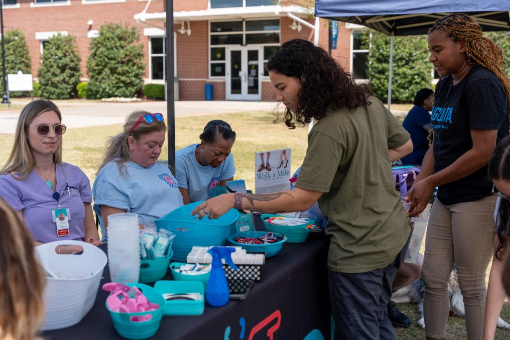 At an outdoor tabling event, a college-aged woman grabs items off of the table.