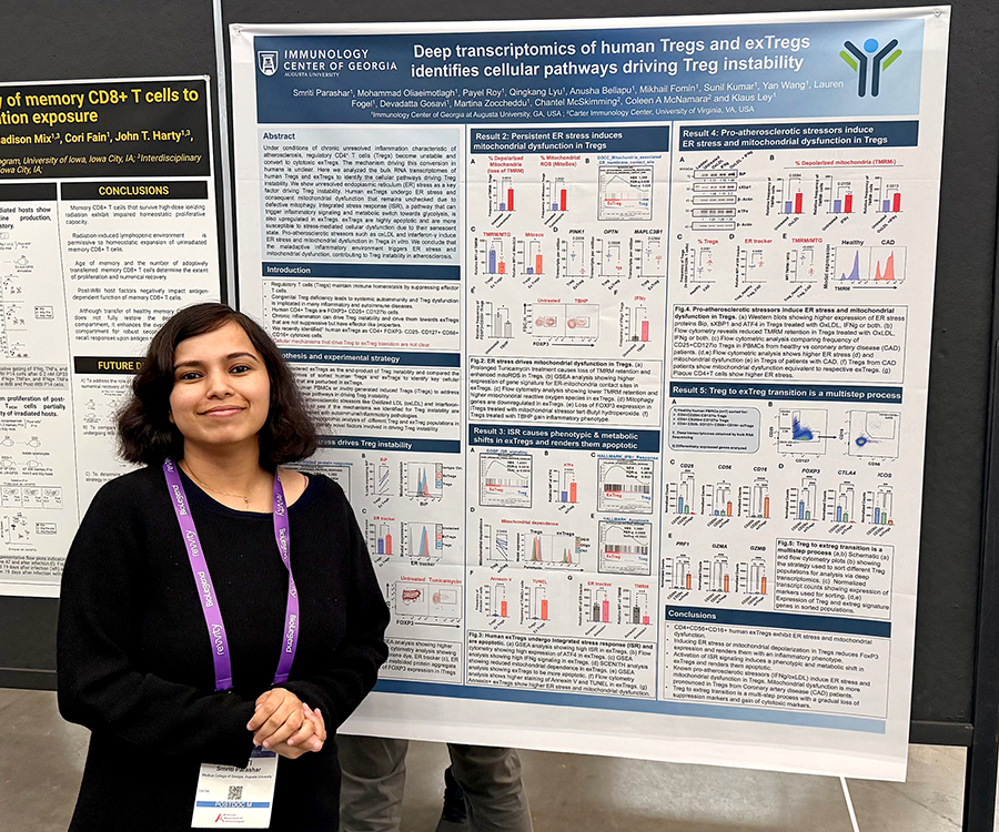 A woman stands beside her scientific poster during a poster session at a large conference.