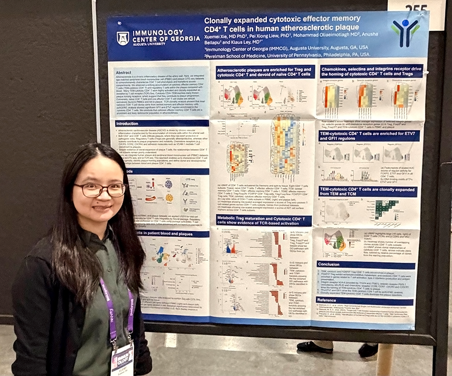 A woman stands beside her scientific poster during a poster session at a large conference.