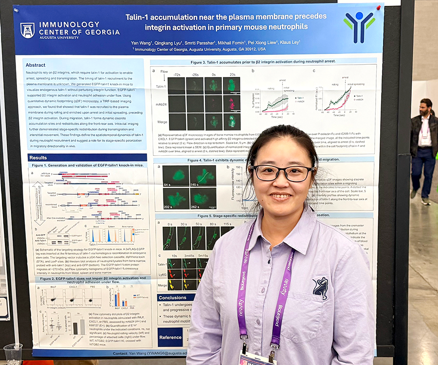 A woman stands beside her scientific poster during a poster session at a large conference.