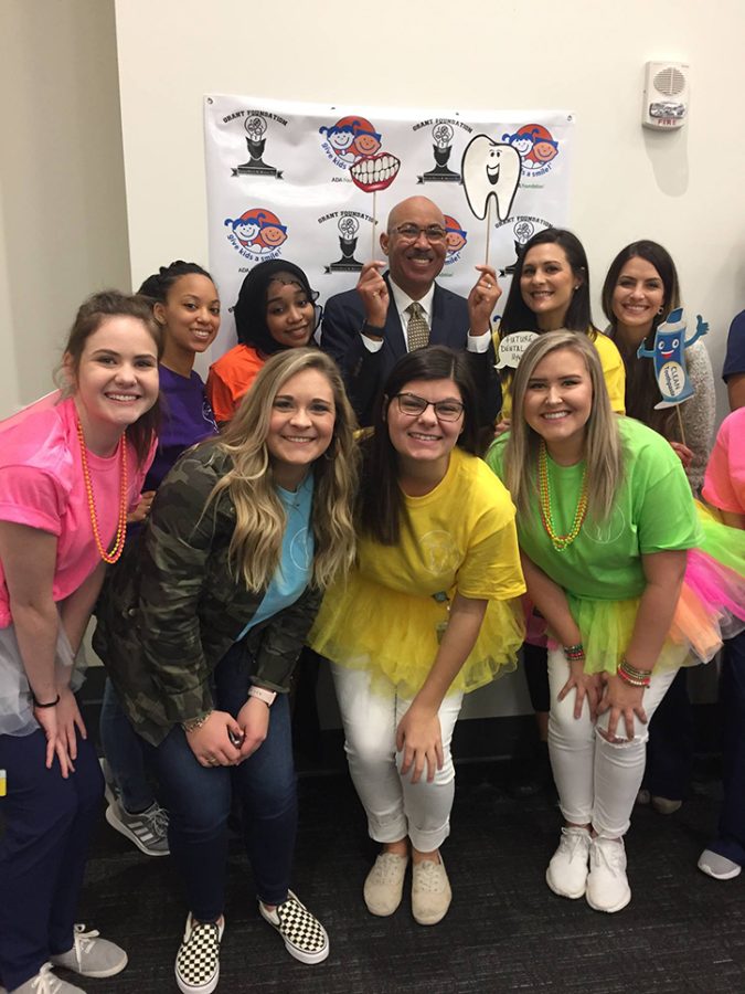 A man holds a mouth sign and tooth smiling with a group of students at a clinic