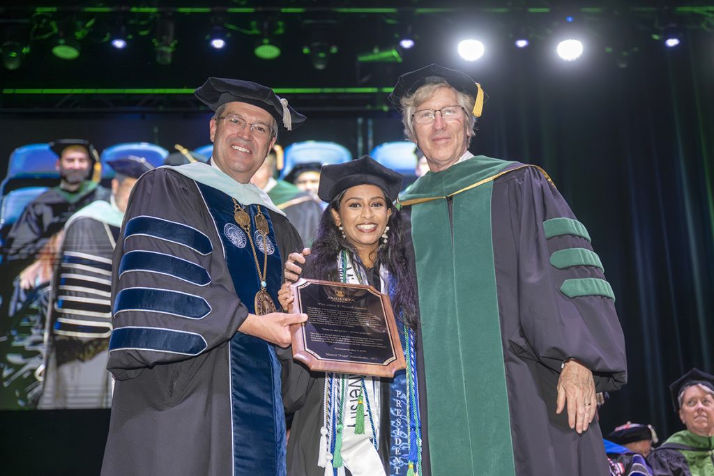 Two men flank woman holding award