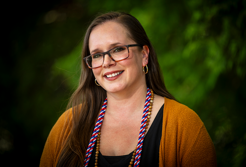 A woman wearing glasses and graduation cords smiles at the camera.