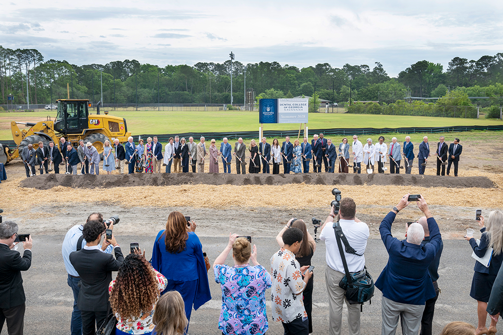 A large group of people stick shovels in dirt at a ceremony.