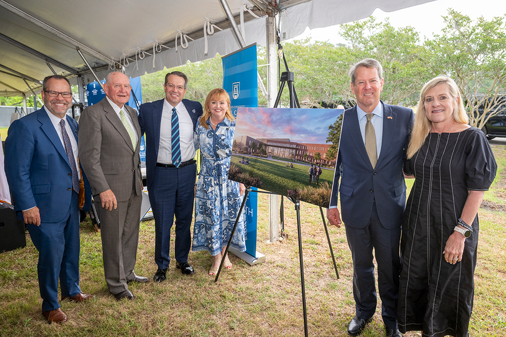 A group of well-dressed people stand around a rendering of a building.