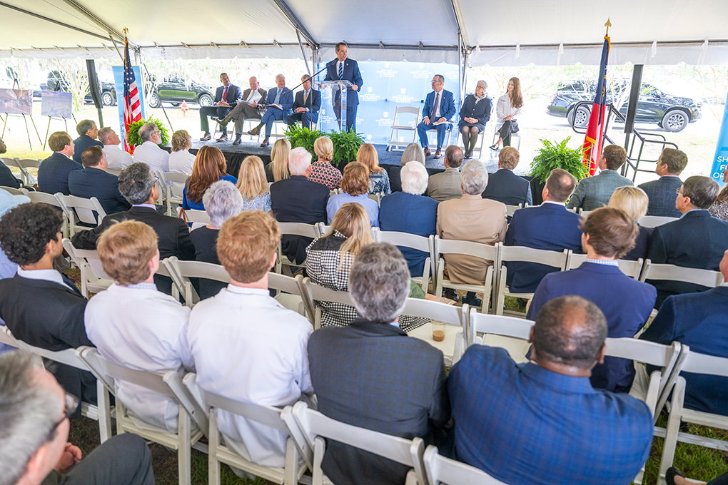 A crowd sits and watches people on a stage speak at a podium.