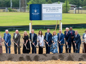 A group of nicely dressed people shovel dirt and smile at the camera.