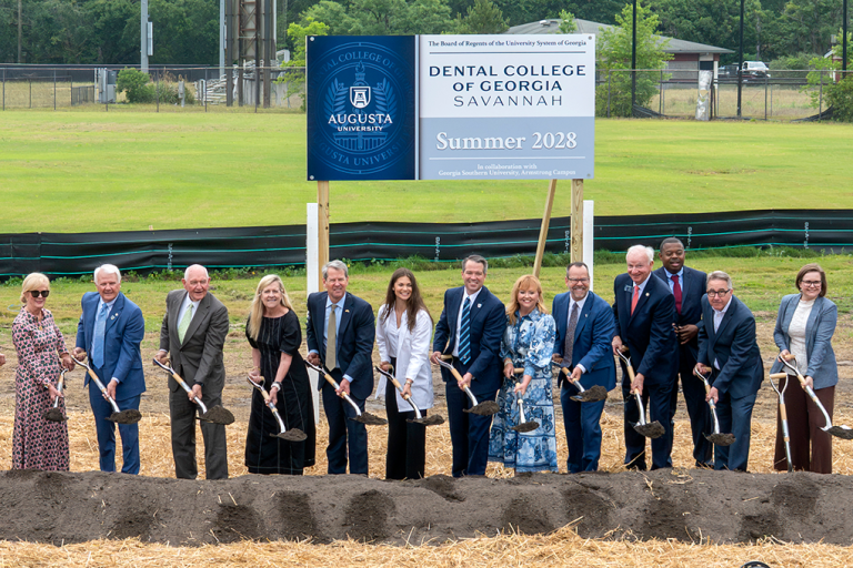 A group of nicely dressed people shovel dirt and smile at the camera.