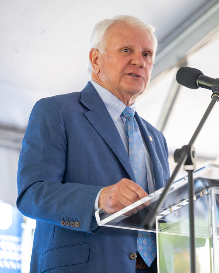 A man in a suit stands behind a podium and delivers a speech.