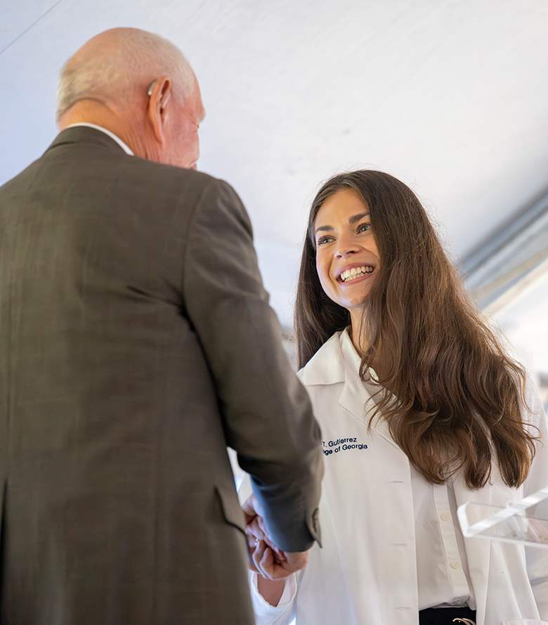 A smiling woman wearing a lab coat shakes an older man's hand.