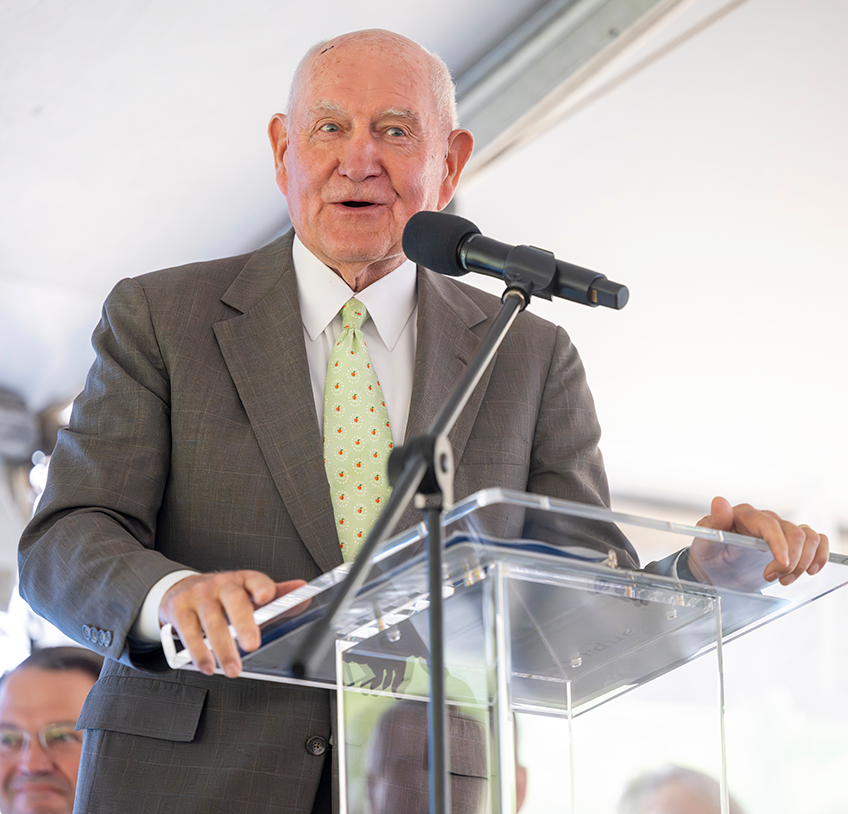 A man in a suit stands behind a podium and delivers a speech.