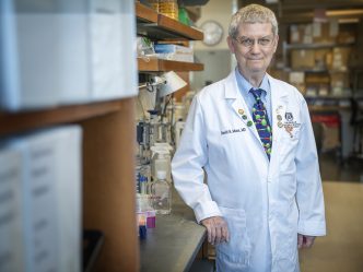 A man in a white coat standing in a lab