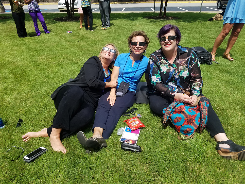 Three women sitting on grass looking into the sky