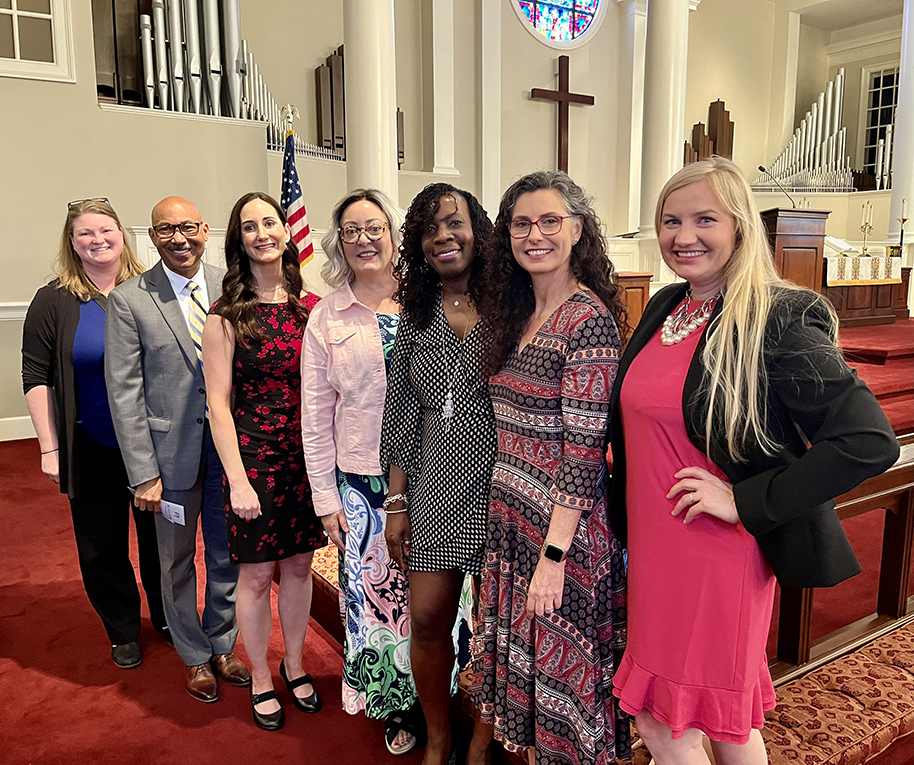 Six women and a man stand in a church getting their photo taken