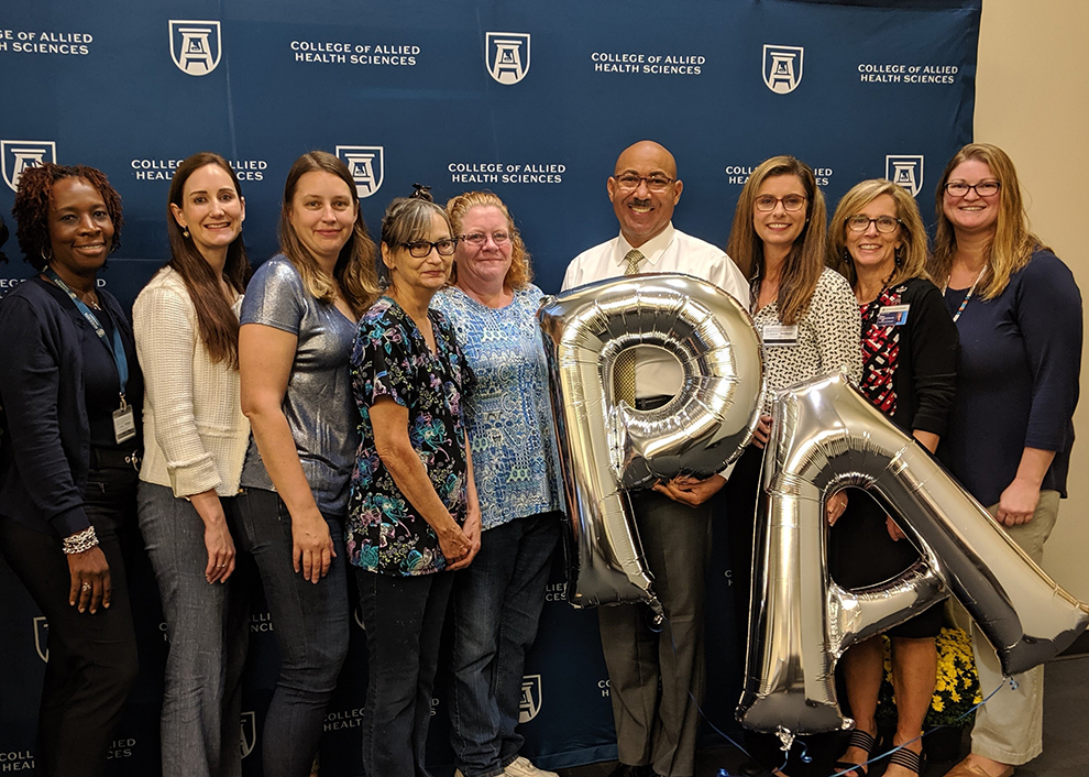A man standing with eight women holding a P and A balloon