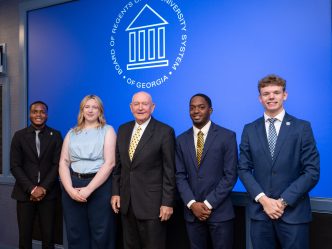 A group of five attendees, including four men and one woman, stand in front of a backdrop displaying the Board of Regents of the University System of Georgia logo.