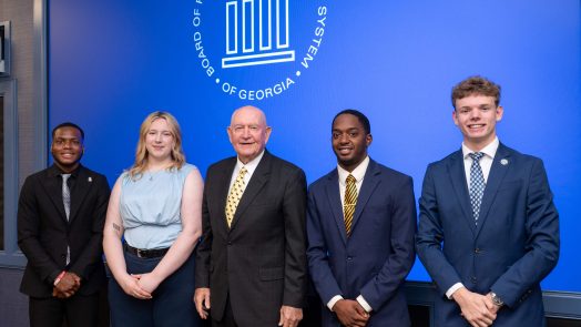 A group of five attendees, including four men and one woman, stand in front of a backdrop displaying the Board of Regents of the University System of Georgia logo.