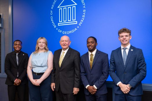 A group of five attendees, including four men and one woman, stand in front of a backdrop displaying the Board of Regents of the University System of Georgia logo.