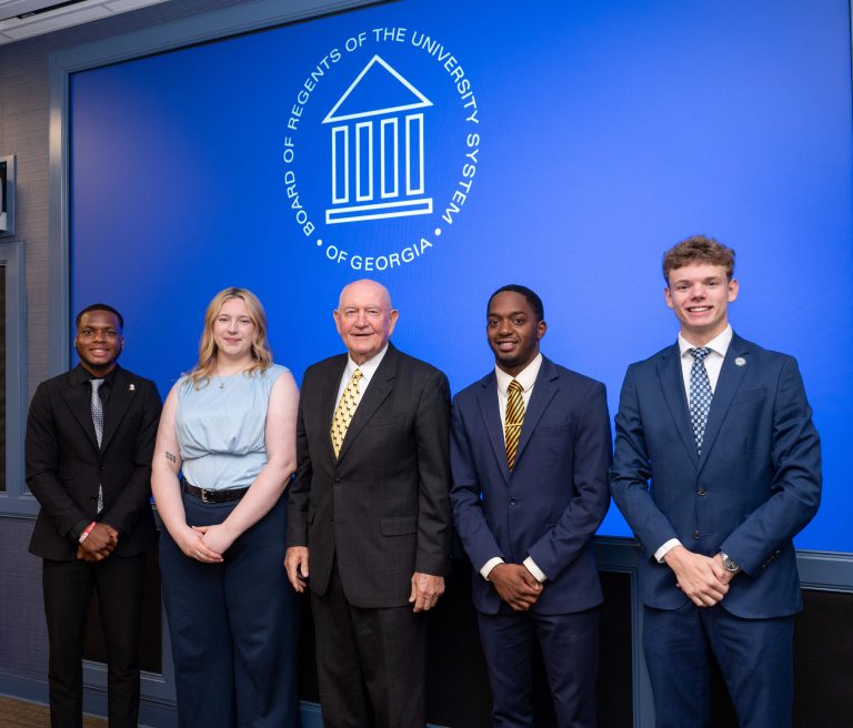 A group of five attendees, including four men and one woman, stand in front of a backdrop displaying the Board of Regents of the University System of Georgia logo.