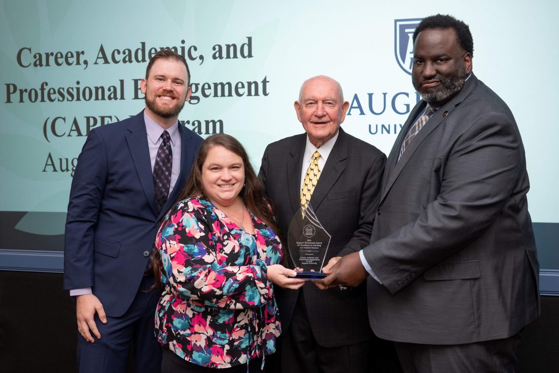 Three men and one woman holding a glass award between them
