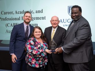 Three men and one woman holding a glass award between them