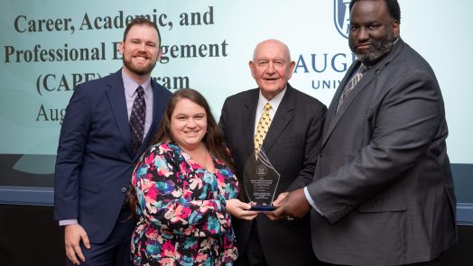 Three men and one woman holding a glass award between them