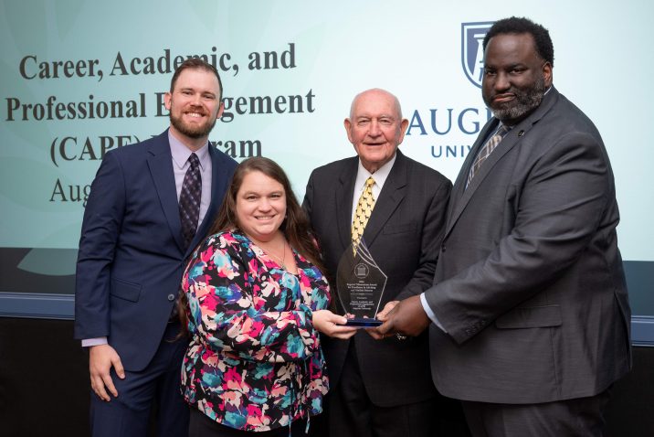 Three men and one woman holding a glass award between them