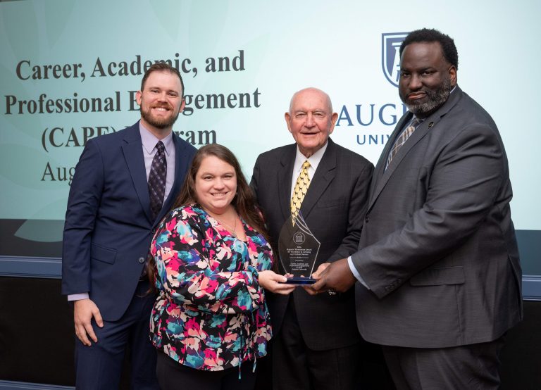 Three men and one woman holding a glass award between them
