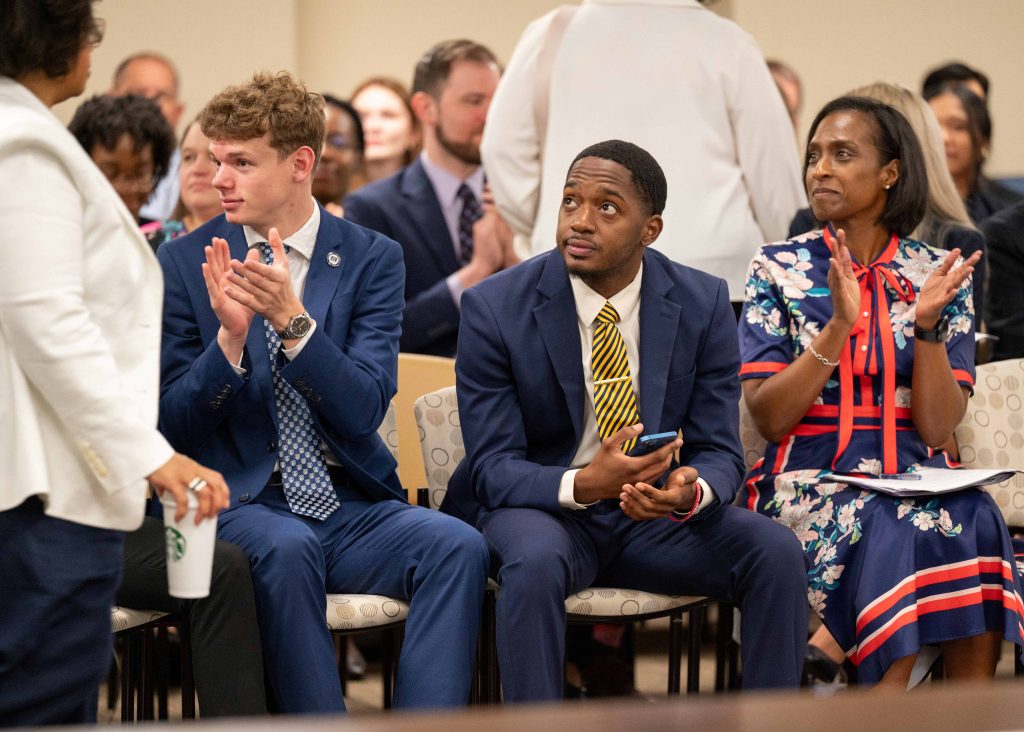 Several men and women clapping while sitting in chairs.