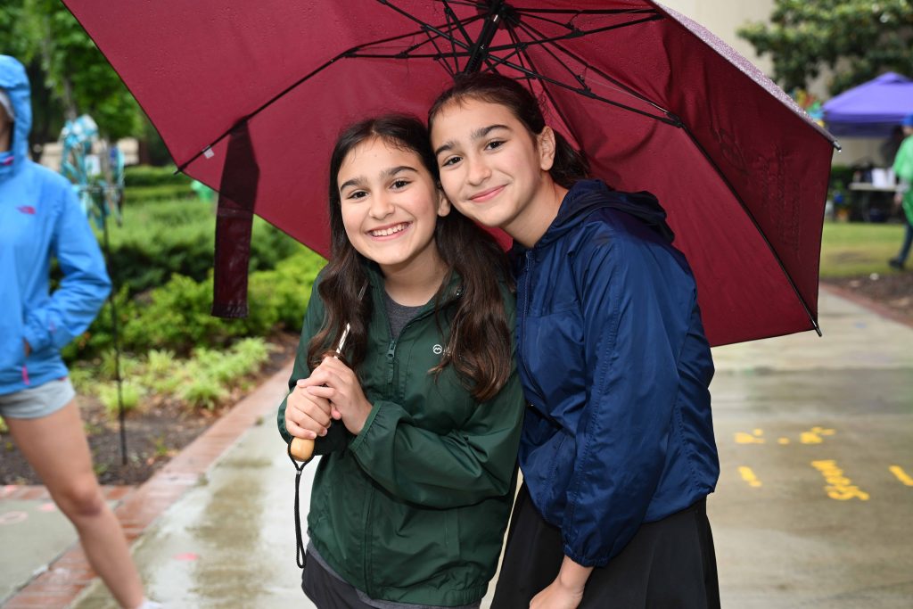 In this photo, you see two girls standing and posing for the picture. One girl is holding an umbrella because it is raining.