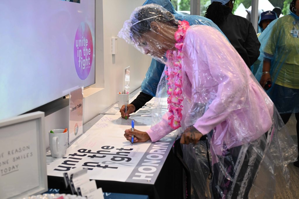 In this photo, you see a female signing a giant white banner. The woman is wearing a clear-colored poncho.