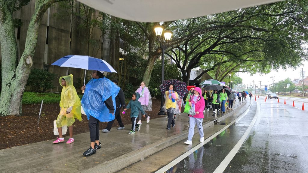 In this photo, you see people walking down a street. The people are participants in the Georgia Cancer Center's Unite in the Fight Against Cancer 2026 community event.