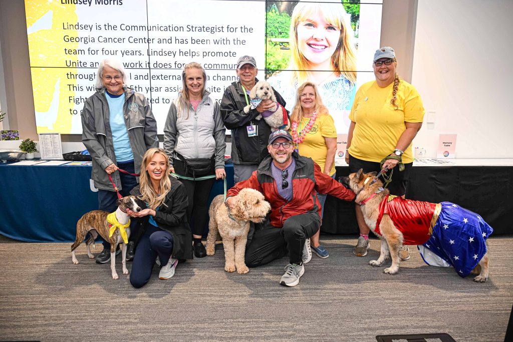 In this photo, you see people posing for the picture while holding dog leashes. One of the dogs is dressed up like the Wonder Woman superhero.