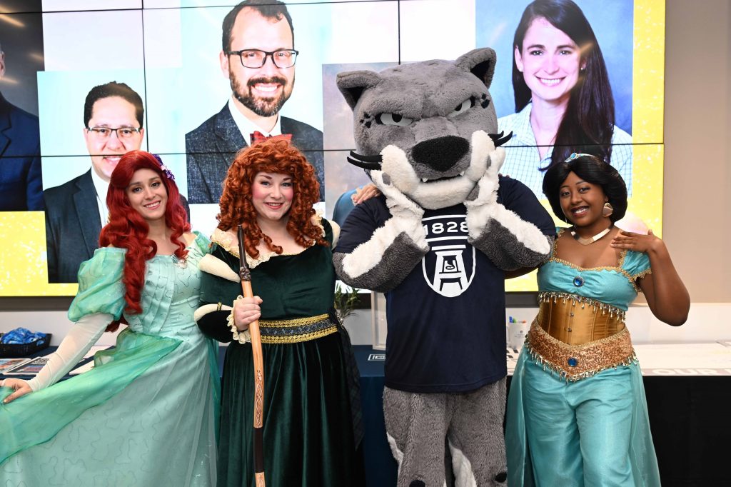 In this photo, you see Augustus, Augusta University's Jaguar mascot, posing for a photo with a group of Disney princesses including Ariel, Jasmine, and Merida.
