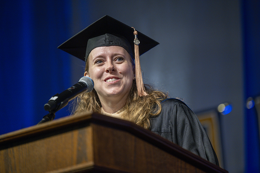 a woman in a graduation robe speaking at a podium 