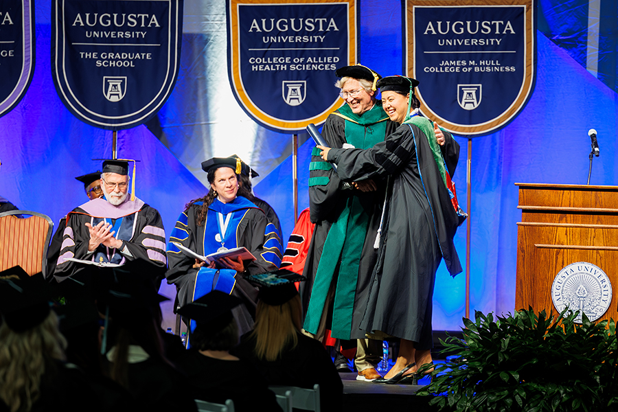 a man and woman wearing graduation robes hug each other. 