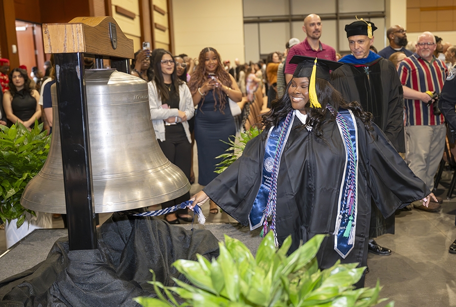 a female student in a graduation robe rings a big silver bell