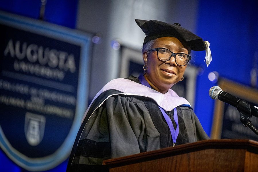 woman wearing a graduation cap and gown speaks at a podium.