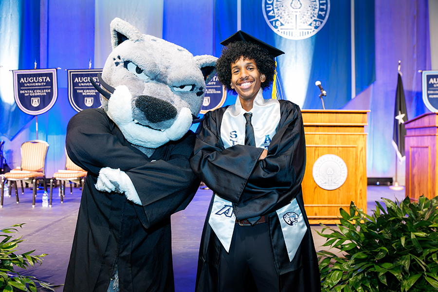 a male student crosses his arms and stands next to a cat mascot
