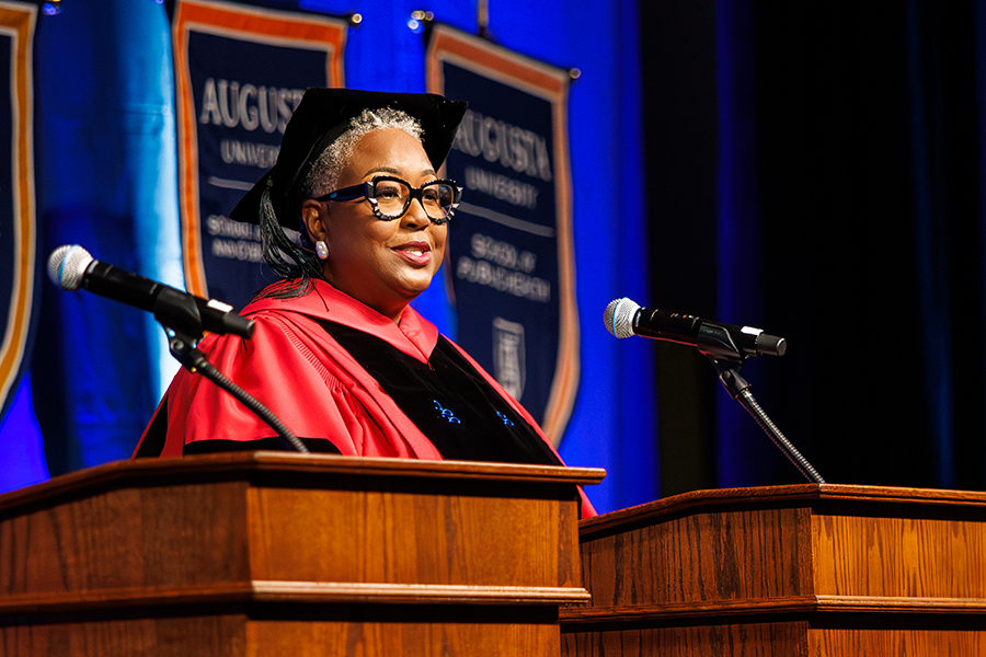 woman in a black and red graduation gown and black rimmed glasses stands at a podium