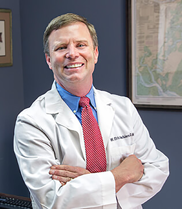 A man wearing a lab coat and a tie smiles at the camera.