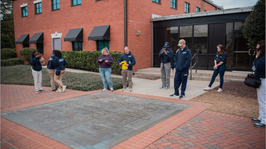 Eight people gathered around a medal mural on the ground