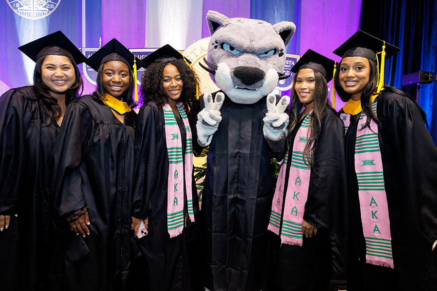 five female students stand next to a cat mascot 
