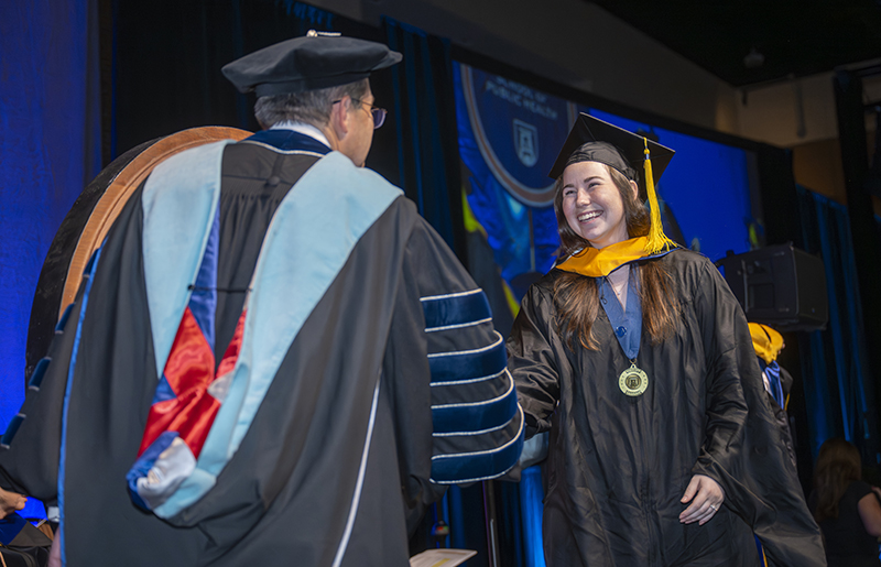 a man and woman in graduation robes shake hands