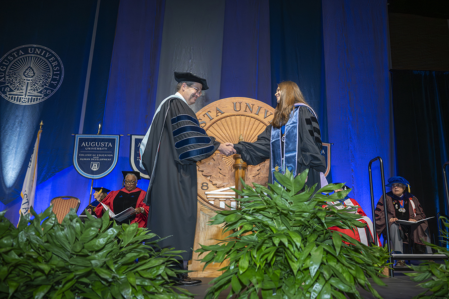 a man and woman wearing graduation robes shake hands