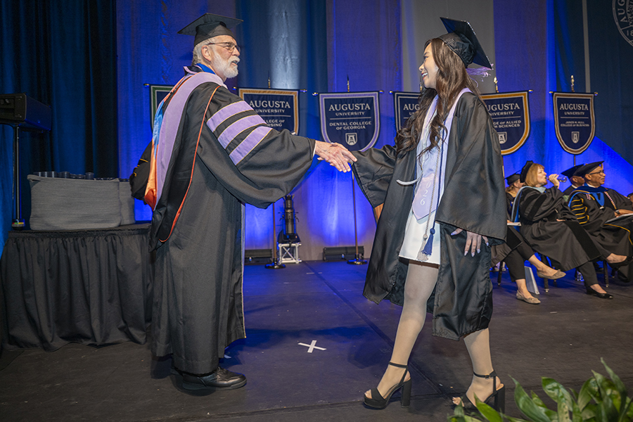 a male and female in graduation robes shaking hands 