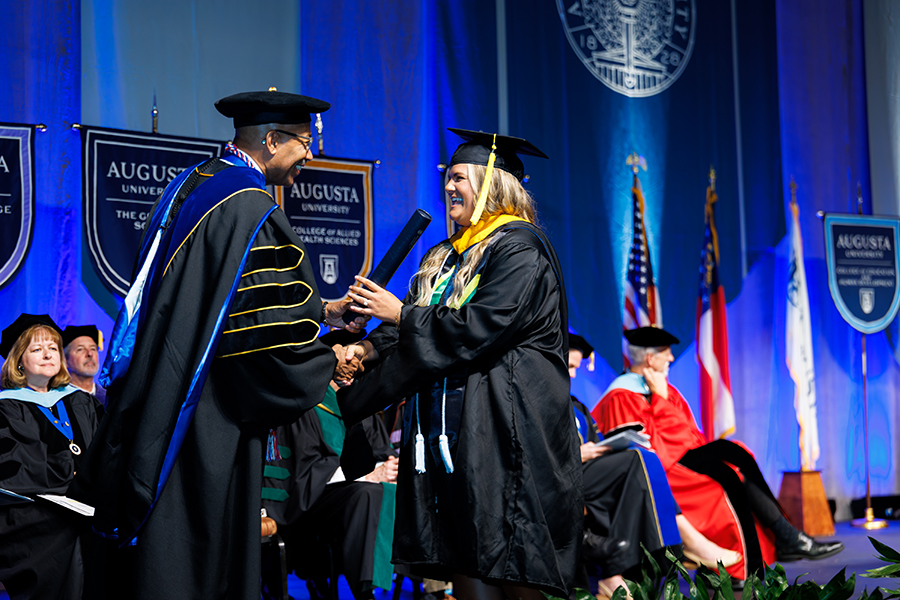 a man and woman wearing graduation robes shake hands