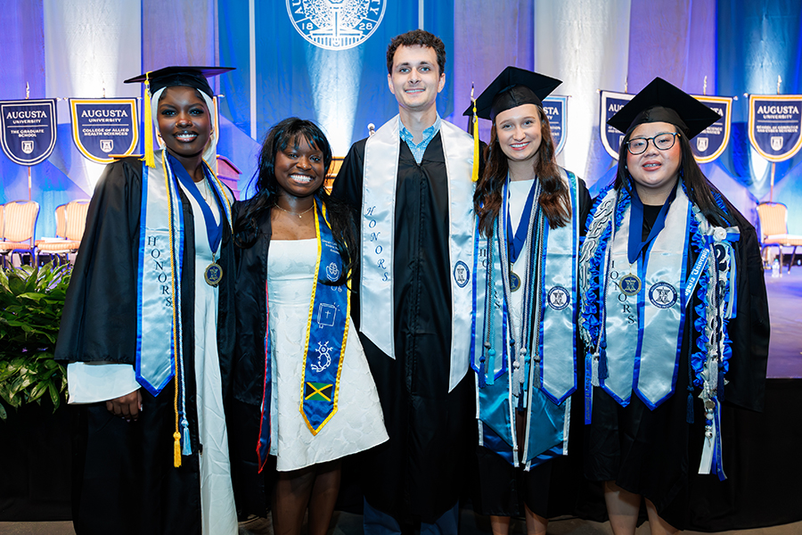 one male student and four female students standing next to each other in graduation robes. 