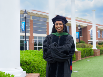 A graduating female student is smiling with four white pillars in the background