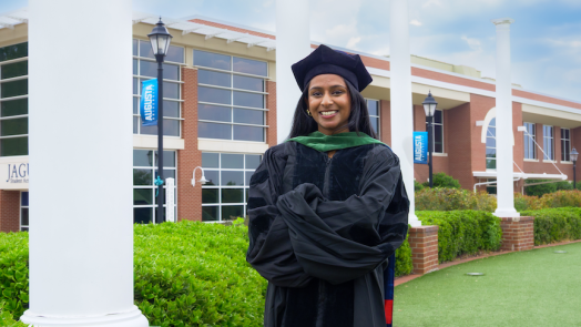 A graduating female student is smiling with four white pillars in the background